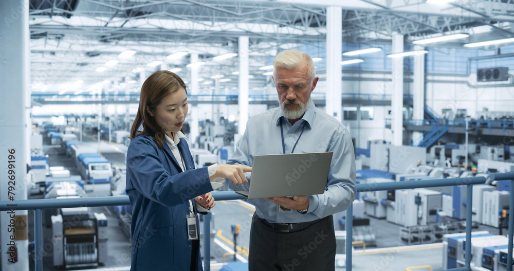 Fototapete Male Engineer and Female Project Manager Standing on a Platform, Talking, Using Laptop Computer and Monitoring Production at a Modern Automated Electronics Manufacture with AI Robots