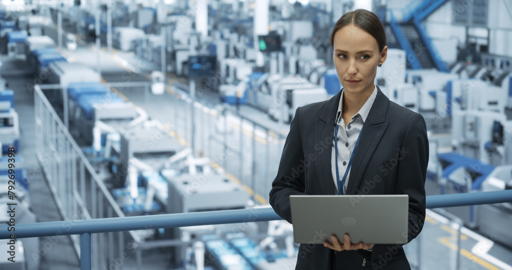 Poster Portrait of a Caucasian Female Engineer Using Laptop Computer and Looking Around a Factory Facility with Robotic Arms Producing Modern Electronic Components for Tech Industries