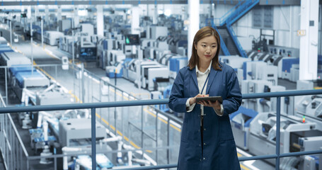 Thoughtful Asian Engineer Monitoring and Analyzing Conditions at a Pristine Modern Electronics Factory with Automated Robot Hands Working with the Help of Artificial Intelligence Software