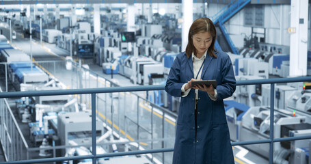 Japanese Factory Manager Working on a Tablet at a Futuristic Industrial Manufacture with Autonomous...