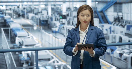 Fototapeta premium Thoughtful Asian Engineer Monitoring and Analyzing Conditions at a Pristine Modern Electronics Factory with Automated Robot Hands Working with the Help of Artificial Intelligence Software