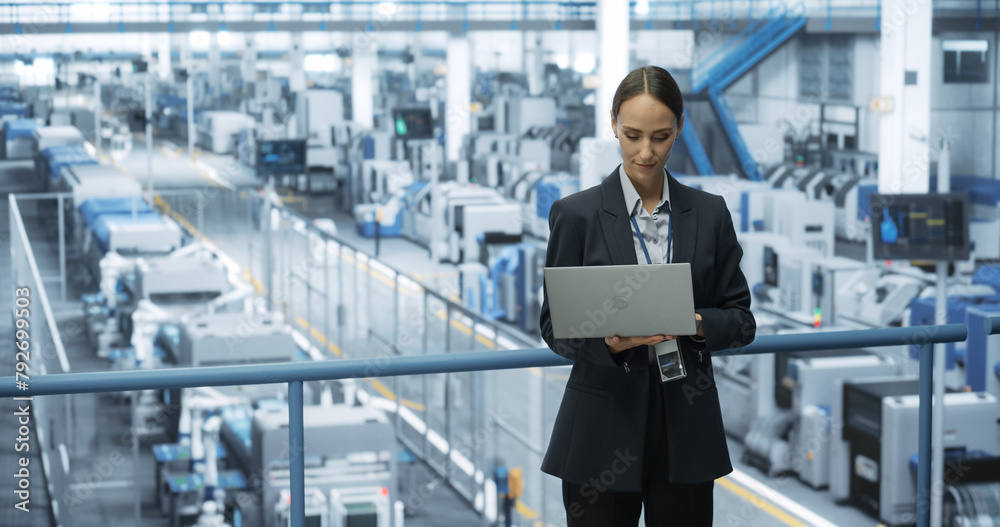 Poster Portrait of a Caucasian Female Engineer Using Laptop Computer and Looking Around a Factory Facility with Robotic Arms Producing Modern Electronic Components for Tech Industries