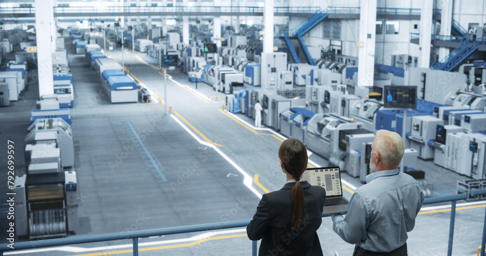 Poster Male Engineer and Female Project Manager Standing on a Platform, Talking, Using Laptop Computer and Monitoring Production at a Modern Automated Electronics Manufacture with AI Robotic Arms