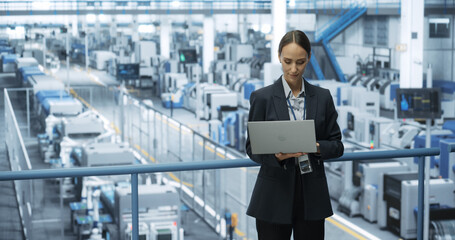 Portrait of a Caucasian Female Engineer Using Laptop Computer and Looking Around a Factory Facility...