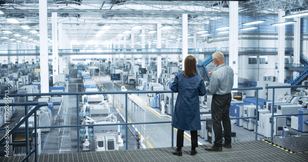 Aufkleber middle aged engineer and female scientist using laptop computer and talking in a factory facility wi