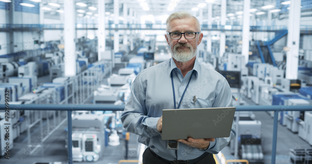 Poster Portrait of a Senior Technician with a Beard and Glasses Using Laptop Computer and Looking at Camera. Industrial Male Specialist Wearing a Protective Vest, Working in a Modern Electronics Factory