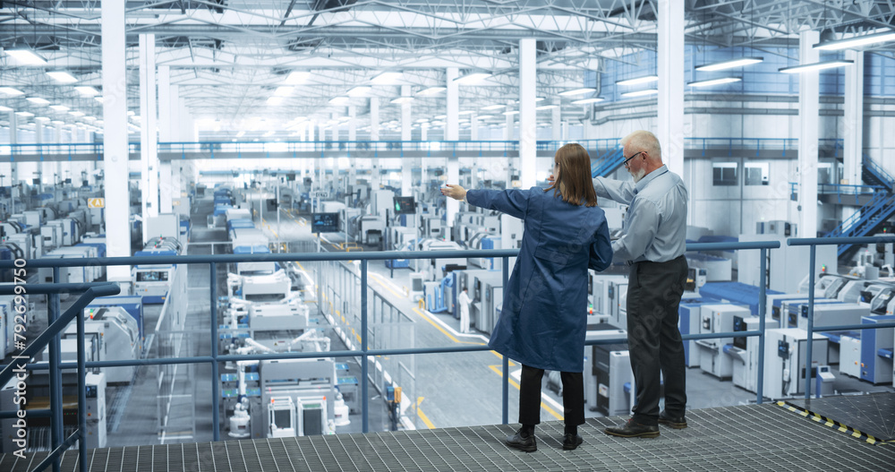 Poster Experienced Male and Female Engineers Standing on a Platform with Their Back to Camera, Using Laptop Computer and Discussing Production at a Modern AI Automated Electronics Manufacture