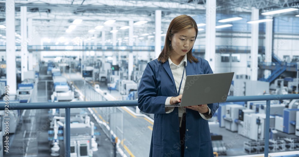 Poster Thoughtful Asian Engineer Monitoring and Analyzing Work at a Modern Electronics Factory with Automated Robot Hands Making Devices. Female Work Colleague Passing By with a Tablet Device