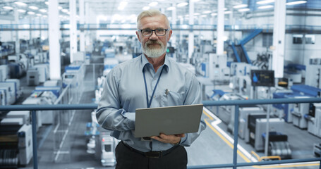 Portrait of a Handsome Middle Aged Engineer Wearing Glasses, Using Laptop Computer and Looking at Camera. Technician in High-VIsibility Vest Working in a Modern Technology Factory - 792699705