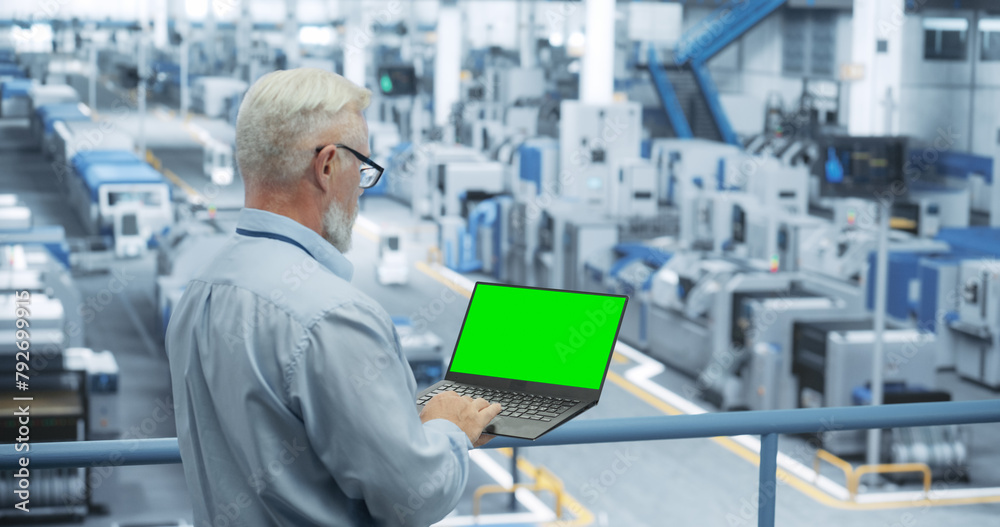 Poster Technician Using Laptop Computer with Green Screen Chromakey Mock Up Display and Looking Around a Factory Facility with Modern Machines Producing Electronic Components for Tech Industries