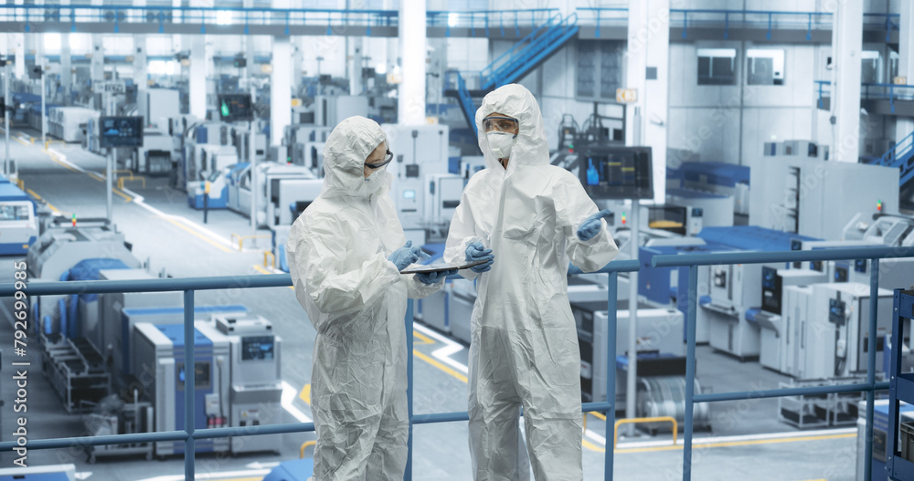 Poster female workers wearing full-body polypropylene coveralls at a manufacturing plant. specialists using