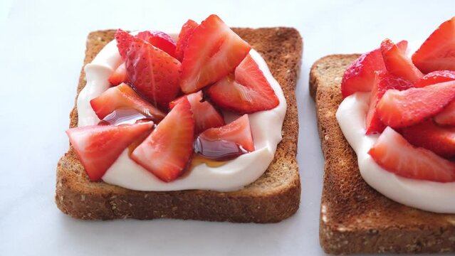 Crispy breakfast toast with ricotta, strawberries and almonds on a white marble background.