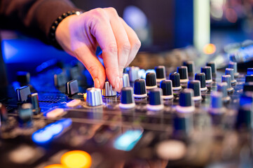 DJ’s hand skillfully adjusting knobs on a vibrant, illuminated mixing console, embodying the spirit of live music production