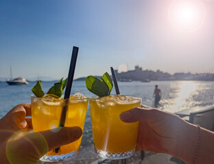 Hands toasting cocktail glasses in front of sea, blue sunny sky background in Bodrum-Turkey, copy...