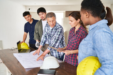 Senior architect discussing blueprint at desk with coworkers in meeting