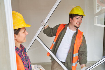 Smiling male carpenter carrying window frame by female coworker at incomplete house site