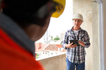 Senior male supervisor with tablet PC looking at female worker standing at incomplete house site