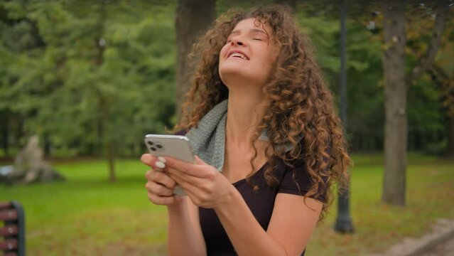 Happy amazed Caucasian woman young girl blogger influencer looking at mobile screen win prize achieve workout goals good results of sport training on smartphone app kissing phone rejoice in city park
