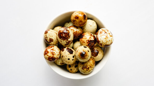 quail eggs in ceramic bowl over white background