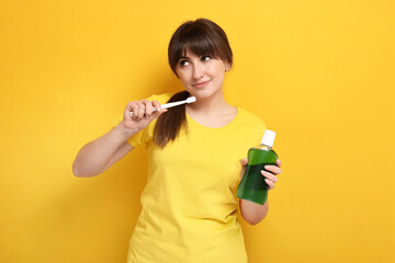 Young woman with mouthwash and toothbrush on yellow background