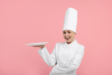 Happy professional confectioner in uniform holding empty plate on pink background