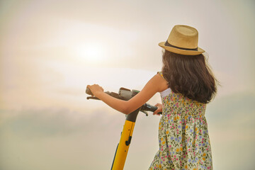 A girl wearing a straw hat is riding a scooter. Summer time