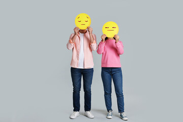 People covering faces with sad emoticons on grey background