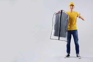 Dry-cleaning delivery. Happy courier holding garment cover with clothes and showing thumbs up on...