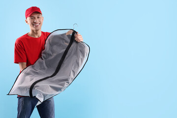 Dry-cleaning delivery. Happy courier holding garment cover with clothes on light blue background,...