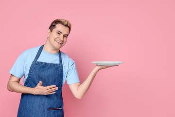 Portrait of happy confectioner holding empty plate on pink background, space for text
