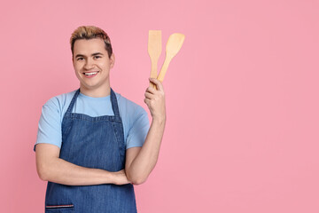Portrait of happy confectioner holding wooden spatulas on pink background, space for text