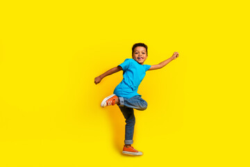 Full size photo of multiethnic multinational little schoolboy wear blue t-shirt denim pants fly arm up isolated on vivid yellow background