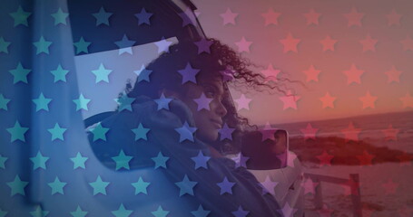 Image of blue and red stars over biracial woman sitting in car - Powered by Adobe