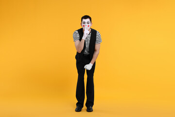 Funny mime artist showing hush gesture on orange background