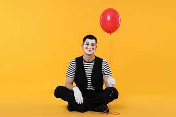 Funny mime artist with balloon on orange background
