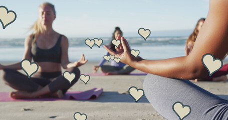 Image of yellow hearts over women practicing yoga on beach