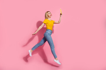 Full length photo of excited funky lady dressed yellow t-shirt jumping tacking selfie device empty space isolated pink color background