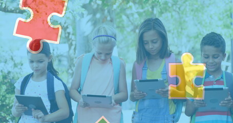 Image of colourful puzzle pieces over school children using tablets