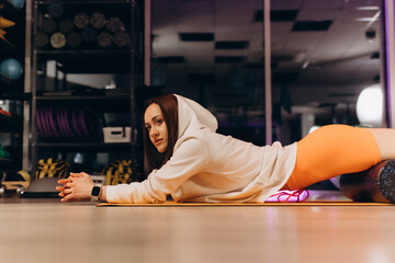 Muscular young athletic woman with perfect beautiful body in sportswear using foam roller massager...