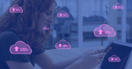 Image of pink clouds uploading data over caucasian businesswoman using smartphone and laptop - obrazy, fototapety, plakaty
