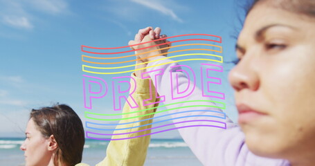 Image of pride flag over diverse lesbian couple holding hands by the sea - obrazy, fototapety, plakaty