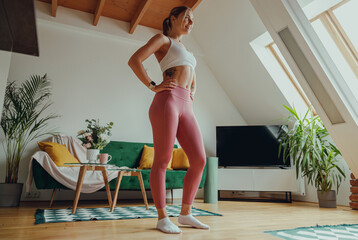 Smiling woman is standing in a living room with her hands on her hips