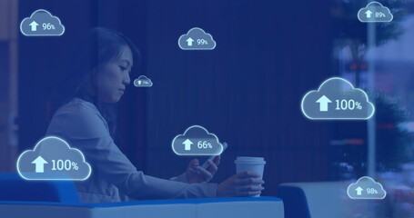 Image of cloud symbols uploading data over asian businesswoman using smartphone at cafe