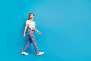 Fototapeta na wymiar Full length profile portrait of lovely girl walk empty space ad wear top isolated on blue color background