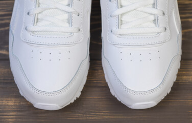 Modern White Classic Leather Sneakers or Trainers on wooden background.