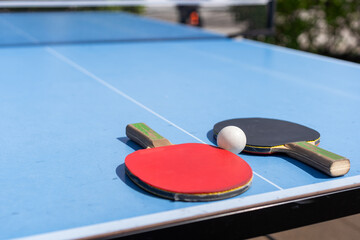Red and black Table Tennis Paddles and ball on the blue table tennis table with net. Ping Pong concept with copy space