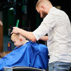 Barber using comb and shaver to cut hair. Professional hairdresser shaving little kid's nape.