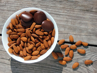 Almonds and dark chocolate in a bowl on a wooden table. Healthy snack.