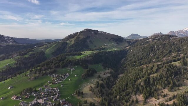 Beauty of rural life with this drone footage capturing majestic mountains, tall trees, green grass, and charm of village nestled under blue sky adorned with fluffy white clouds at Amden Sentis Schweiz