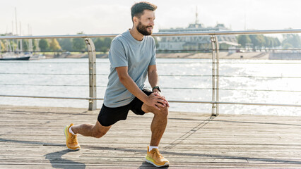 A bearded athlete lunges forward on a sunlit pier with a relaxed smile, boats and a marina forming a serene backdrop.